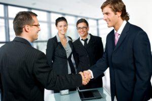Businesspeople shaking hands in a modern office - OutsourceExecs.com